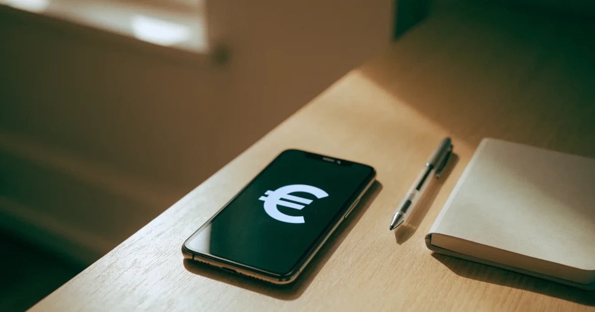 Ein Smartphone liegt neben einem Notizbuch und einem Kugelschreiber auf einem hellen Schreibtisch, das Display ist ausgeschaltet.