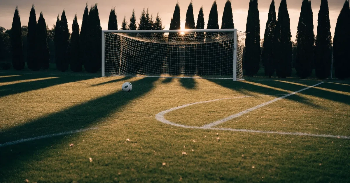 Ein Fußballtor mit Netz auf einem leeren Platz im Abendlicht, der Rasen frisch gemäht, im Hintergrund Zypressen.
