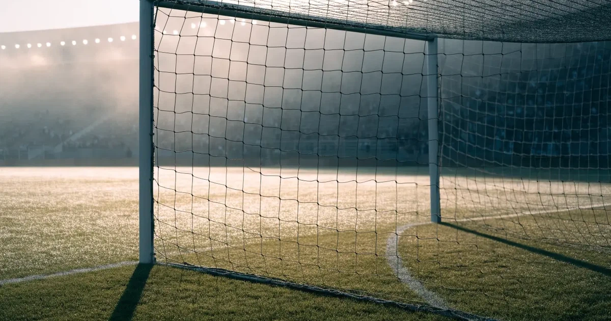 Ein Fußballtor mit Netz steht auf einem leeren Platz im Nebel der Morgendämmerung, der Rasen ist taufeucht.