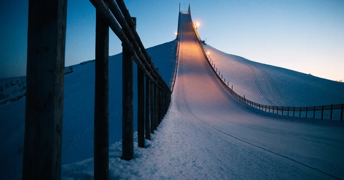 Eine Skisprungschanze im Schnee, von unten gesehen, vor einem klaren Winterhimmel in der Dämmerung, ohne Menschen.