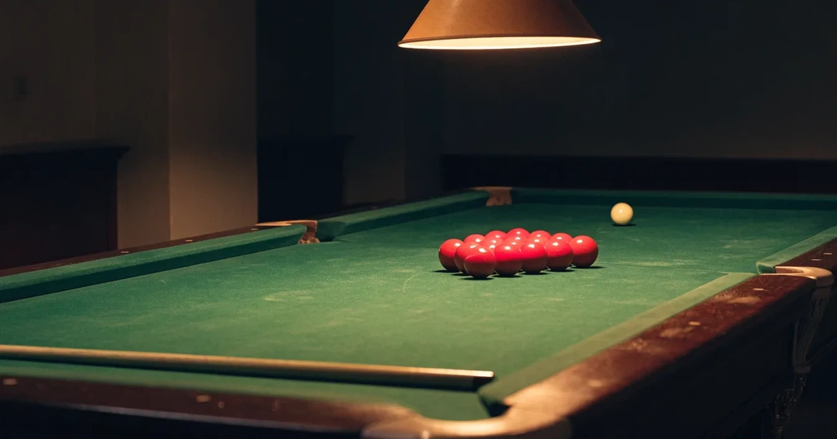 Ein Snookertisch mit grünem Tuch und aufgebauten roten Kugeln in einem abgedunkelten Raum unter einer hängenden Lampe.