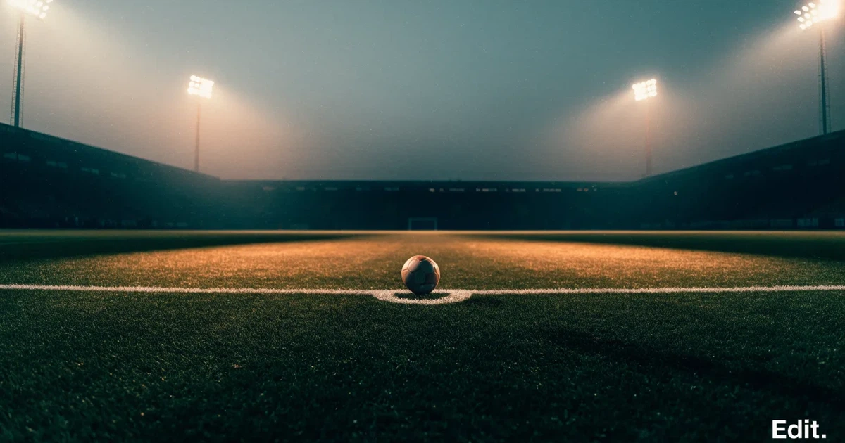 Ein Rasenplatz in der Dämmerung mit eingeschalteten Flutlichtmasten, ein Ball liegt am Anstoßpunkt, die Tribünen im Hintergrund sind unscharf.